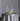 The Hall of Flame Round Table Cluster features a round table with a silver satin tablecloth, gold flatware for four, empty coupe glasses, a white floral centerpiece, and seven long-burning tall white candles in silver holders.
