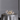 A Hall of Flame Round Table stands out in the room, elegantly covered with a silver satin cloth, gold flatware, two wine glasses, white flowers centerpiece, and Pillar Cluster candles from Hall of Flame, set against a plain gray wall.
