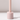 The Hall of Flame Ballet Pink Wax Candle Holder, made from sustainable plant-based wax in a pale pink cylindrical design with a vertical rod, stands on a white surface and casts a soft shadow against a plain light background.