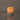 A Hall of Flame Pillar with Wax Sleeve candle sits on a smooth, reflective surface, its warm flame glowing against a plain background.
