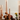 Hall of Flame’s Venti Brown Wax Candle Holders display tall beige candles, arranged with brown roses, green foliage, figs, and a yellow flower for an elegant, warm touch.