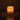 The Hall of Flame Pillar with Wax Sleeve glows warmly in a dark room, its gentle flame illuminating the space and casting a soft reflection on the smooth surface beneath its elegant wax sleeve.