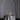 The Hall of Flame Round Table Cluster is elegantly arranged with long burn time white candles, a bouquet, two plates, and two wine glasses atop a shiny white tablecloth before a large ornate white arch.