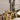A table features Hall of Flame Mini Pillar Glass Sleeves with lit candles, pale dahlias, white orchids, and yellow Buddhas hand citron fruit, all set against a neutral wall with architectural details.