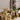 A table features white flowers, a white endive, a green Buddha’s hand citron, and three lit candles in Hall of Flame Mini Pillar Glass Sleeves, all arranged on a white tablecloth against a light background.