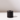 The Hall of Flame Black Wax Candle Holder, crafted from sustainable plant-based wax, features a cylindrical design with a central hole. It sits on a glossy white surface, casting a soft shadow against a plain, softly lit background.