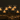 The Hall of Flame Floating Candle Trio Set, lit in clear water-filled vases and arranged on a dark table with brown plates and cutlery, creates a warm, elegant ambiance—ideal for wedding events.