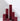 Six Hall of Flame Bordeaux Dark Red burgundy Square Pillar Candles are clustered on a white surface, their burgundy colour.