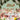 An elegant event features pastel chairs, flower-adorned tables, Hall of Flame Sky Blue Taper Candles XXL, glassware, and a mint green scalloped backdrop with floral decorations and gold script, plus greenery on the walls.