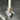 A Hall of Flame Mini Flower Object displays a white pillar candle upright in a translucent, flower-shaped holder with ruffled petals, ideal for ornamental use and placed on a shiny metal surface casting a soft shadow.