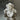 The Hall of Flame Mini Flower Object, a white ruffled decorative sculpture with a pearly sheen, rests on a reflective metallic surface, casting a gentle shadow below.
