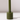 The Hall of Flame Moss Green Wax Candle Holder, a sustainable plant-based cylindrical piece with a tall, thin stem, stands on a white surface casting a faint rightward shadow against a softly lit plain background.