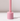 The Hall of Flame Petal Pink Wax Candle Holder features a cylindrical, glossy design with smooth edges. It stands on a white surface with a vertical rod, casting a soft shadow and offering minimalist elegance.