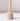 The Hall of Flame Sand Beige Wax Candle Holder, featuring a cylindrical shape and long vertical handle, stands upright on a white surface, casting a shadow to the right.