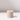 The Hall of Flame Sand Beige Wax Candle Holder, a single plant-based cylindrical piece with a central hole, rests on a white surface and casts a gentle shadow to the right against a plain light background.