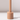 The Venti Brown Wax Candle Holder by Hall of Flame features a cylindrical beige design with a vertical rod on a matching base, casting a shadow on white against a light background.