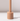 The Venti Brown Wax Candle Holder by Hall of Flame features a cylindrical beige design with a vertical rod on a matching base, casting a shadow on white against a light background.