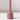 The Hall of Flame Dusty Rose Wax Candle Holder features a minimalistic cylindrical base and tall, narrow stem. It stands on a white surface against a light background, casting a gentle shadow.