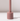 The Hall of Flame Dusty Rose Wax Candle Holder features a minimalistic cylindrical base and tall, narrow stem. It stands on a white surface against a light background, casting a gentle shadow.