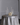 The Hall of Flame Round Table Cluster features a round table with a silver satin tablecloth, gold flatware for four, empty coupe glasses, a white floral centerpiece, and seven long-burning tall white candles in silver holders.