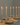 The Hall of Flame Straight Set Bundle features beige plates, silver cutlery, and six tall cathedral candles in disposable wax holders, all arranged on a white tablecloth—ideal for minimalist wedding dining.