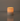 A Hall of Flame Pillar with Wax Sleeve candle sits on a smooth, reflective surface, its warm flame glowing against a plain background.