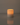 A Hall of Flame Pillar with Wax Sleeve candle sits on a smooth, reflective surface, its warm flame glowing against a plain background.