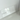 A clear, rectangular Acrylic Candle Drip Tray by Hall of Flame is displayed on a white shelf against a white wall, with the brand name faintly visible and a window reflection on the tray.
