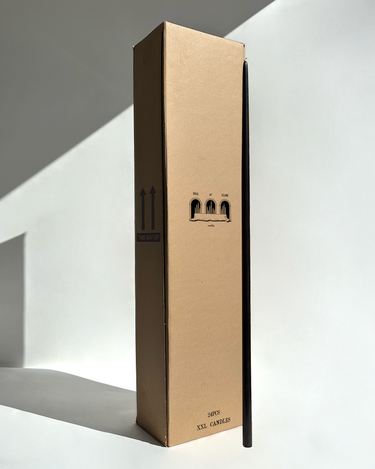 A tall Hall of Flame box labeled Bulk Candles - Wholesale box stands upright beside a single slender black candle.