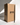 A tall, rectangular Hall of Flame Bulk Candles | Wholesale by-the-box packaging with THIS WAY UP arrows stands upright as a long black taper wedding candle leans against it, casting a shadow on the light background.