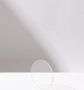 The Hall of Flame Acrylic Base Plate is a clear, thin, circular acrylic sheet that stands upright on a white surface, providing durable tablecloth protection and casting a subtle shadow against a light gray background.