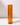 The Hall of Flame Amber | Coloured Glass Sleeves features a tall, orange-tinted candle holder with an amber glass sleeve, elegantly displaying a single upright orange candle against a white background with soft shadows.