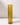 A tall, cylindrical olive-coloured glass sleeve by Hall of Flame holds a matching taper candle, casting soft reflections on a white surface against a plain light background.