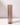 A beige taper candle stands upright in a Hall of Flame Smoke Coloured Glass Sleeve, its tall cylindrical form casting a soft shadow on a white surface against a plain light background.