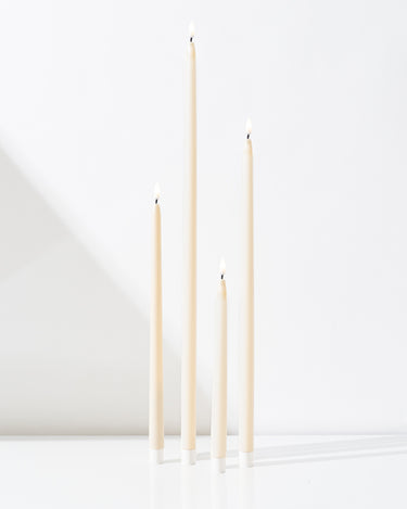 Four Hall of Flame Ivory Ultra-Bright LED Flameless Taper Candles of varying heights stand upright on a white surface against a white background, casting soft shadows.