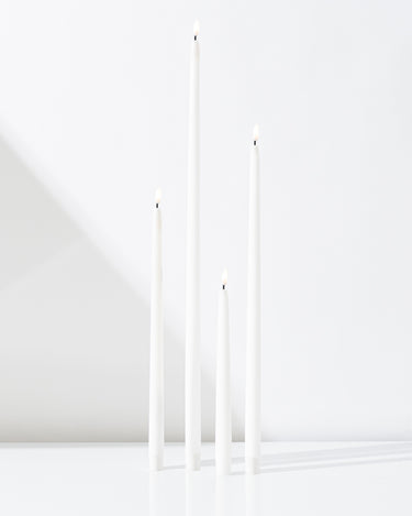 Four Hall of Flame White Realistic LED Flameless Taper Candles of varying heights stand lit and upright on a smooth white surface against a plain white background.