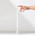 A hand gently touches the top of a Hall of Flame White Realistic LED Flameless Taper Candle, standing upright on a white surface against a white background.