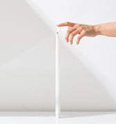 A hand gently touches the top of a Hall of Flame White Realistic LED Flameless Taper Candle, standing upright on a white surface against a white background.
