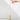 A hand reaches for the flame of a Hall of Flame Ivory Ultra-Bright LED Flameless Taper Candle, displayed in a gold holder on a white surface against a plain white background.