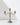 The Hall of Flame 3-arm Antique Gold Candelabra rests on a reflective white surface against a plain light background, its three ornate candle holders casting a soft shadow.