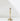 The Hall of Flame Tall | Antique Gold Holder, a single brass candlestick with a slender, elegant design, rests on a white surface. Its classic vintage style and soft shadows highlight its timeless appeal.