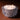 The Hall of Flame Spike Hand Blown Glass Bowl, featuring smooth white wax and three lit wicks, rests on a brown surface as its textured clear glass casts a warm, gentle glow.