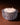 The Hall of Flame Spike Hand Blown Glass Bowl, featuring smooth white wax and three lit wicks, rests on a brown surface as its textured clear glass casts a warm, gentle glow.