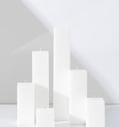 Six Hall of Flame White Square Pillar Candles XXL in various heights are arranged on a white surface.