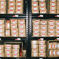 Rows of Hall of Flame Mystery Bundle packages, each marked with white and red tags, are neatly arranged on shelves in a warehouse.