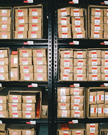 Rows of Hall of Flame Mystery Bundle packages, each marked with white and red tags, are neatly arranged on shelves in a warehouse.