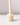 The Hall of Flame Ivory Wax Candle Holder, featuring a beige cylindrical design with a smaller cylinder in a wide base, stands upright and casts a soft shadow on a white surface against a pale background.