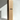 A tall Hall of Flame Bulk Candles | Wholesale by-the-box cardboard box stands upright next to an extra-long pale yellow taper wedding candle, both set against a white backdrop with soft light and shadows.