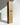 A tall Hall of Flame Bulk Candles | Wholesale by-the-box cardboard box stands upright next to an extra-long pale yellow taper wedding candle, both set against a white backdrop with soft light and shadows.