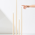 Four Hall of Flame Ivory Ultra-Bright LED Flameless Taper Candles of various heights stand upright on a white surface, while a hand with an extended finger reaches toward the tallest one. The background is plain white.